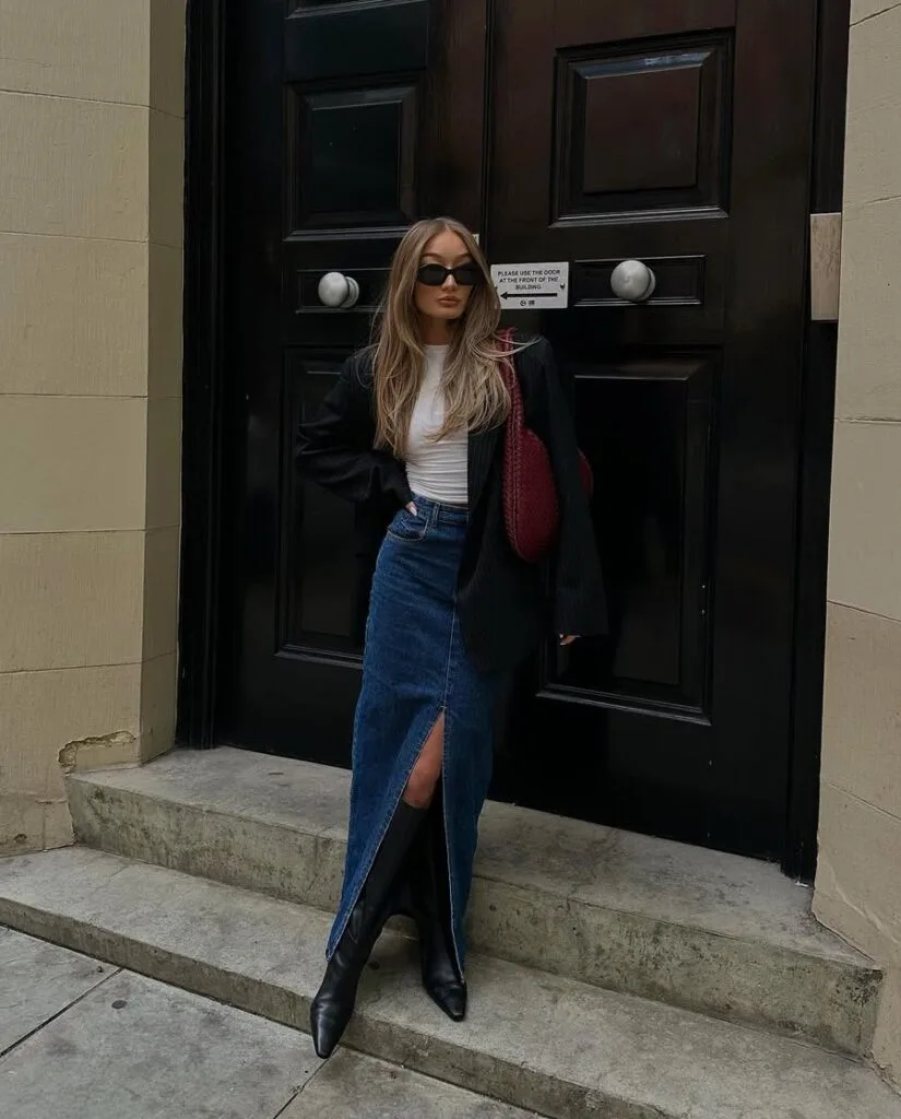 Black blazer with white tee, denim midi skirt with slit, and knee-high boots—chic casual winter outfits.
