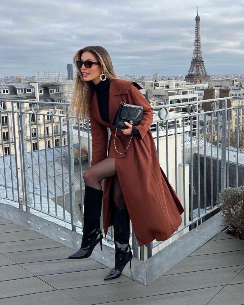 Brown coat and mini dress paired with shiny black tall boots, Statement-Making Long Boots trend, Paris rooftop view.