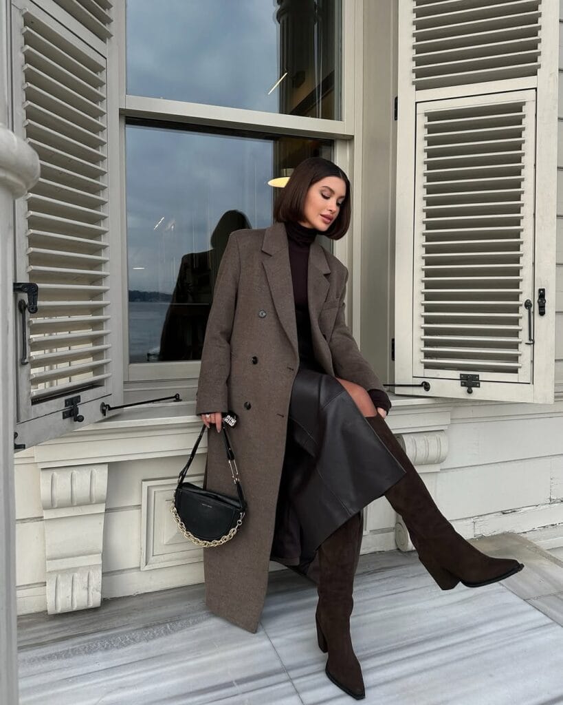 Brown wool coat and chocolate turtleneck styled with tall dark brown boots, Statement-Making Long Boots trend, city balcony.