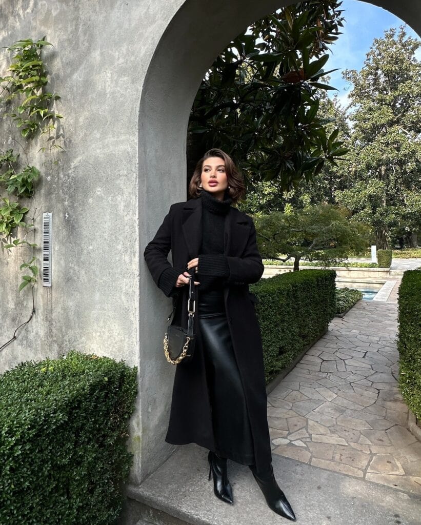 woman in black wool coat, chunky turtleneck, leather midi skirt, boots, gold chain bag, winter outfit
