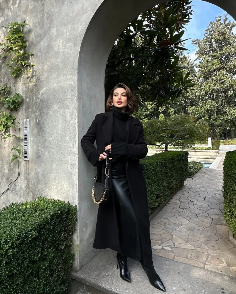 woman in black wool coat, chunky turtleneck, leather midi skirt, boots, gold chain bag, winter outfit