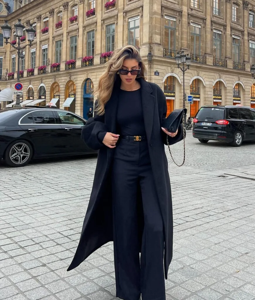 winter work outfit with dark navy coat, navy top, navy wide-leg trousers, black clutch, pointed heels
