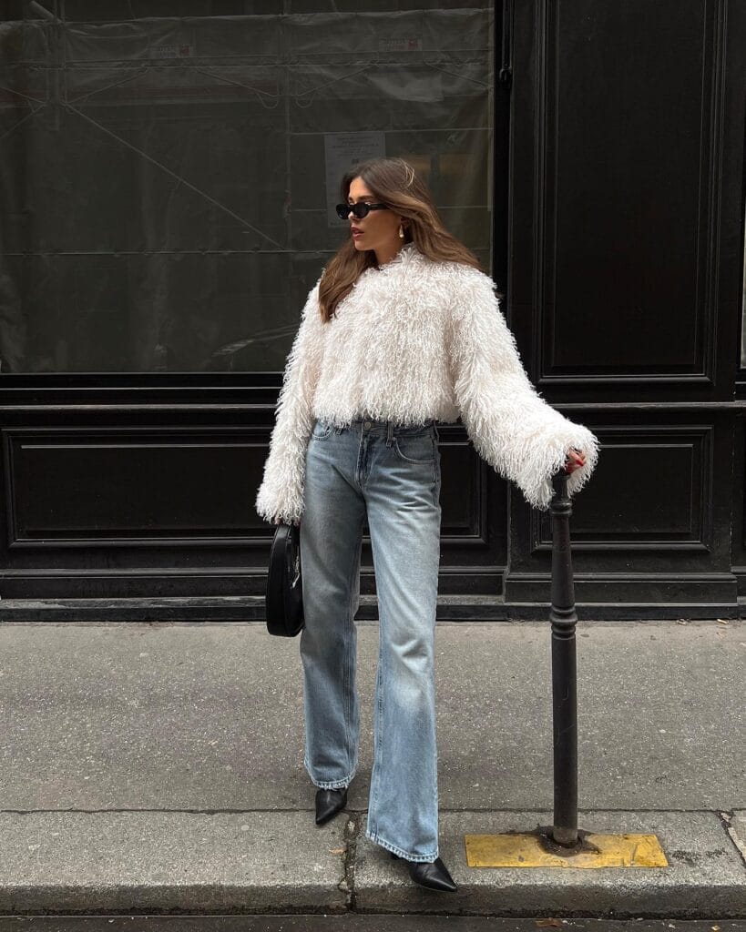 woman wearing cream shaggy sweater, light jeans, and black pointed boots, effortlessly chic winter outfit
