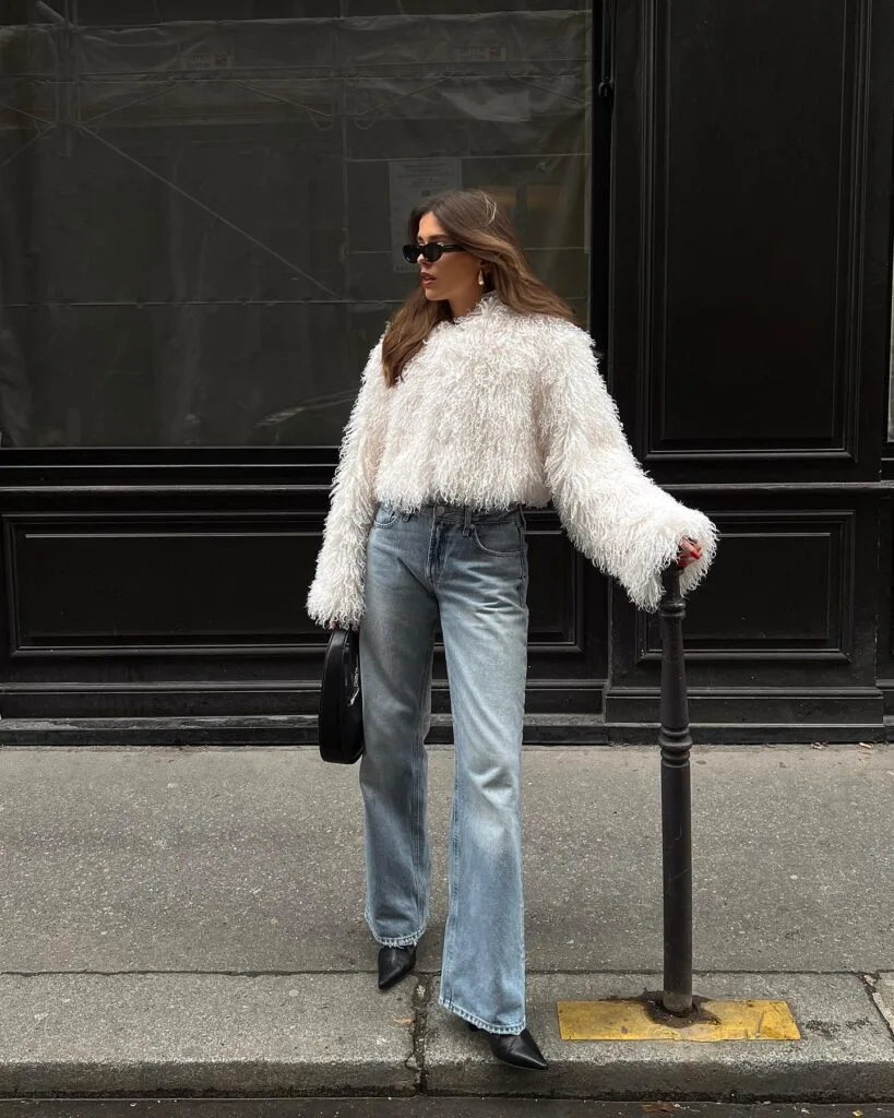 woman wearing cream shaggy sweater, light jeans, and black pointed boots, effortlessly chic winter outfit