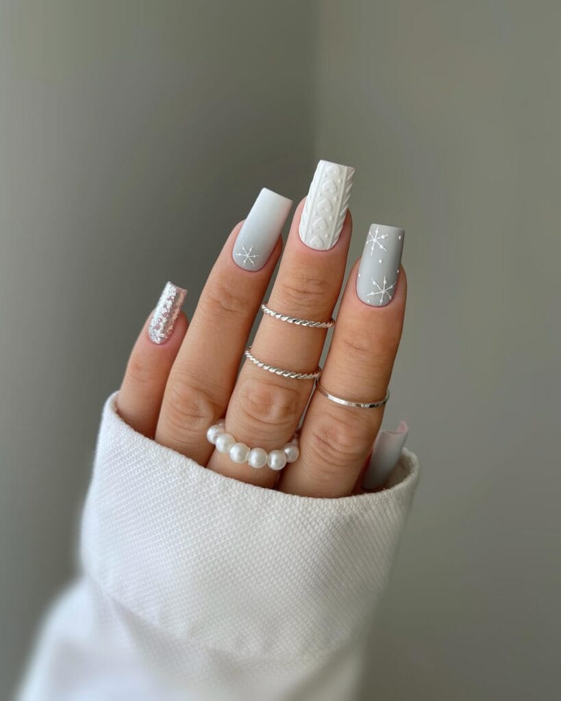 Grey and white January nails with snowflakes, 3D sweater-knit texture, and a rose-gold glitter accent.