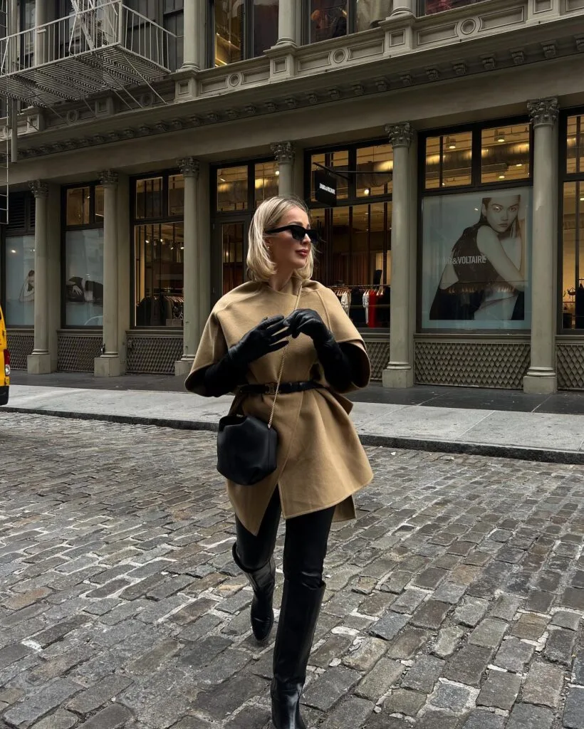 woman in camel cape, black gloves, tall boots, walking on cobblestone street winter outfit
