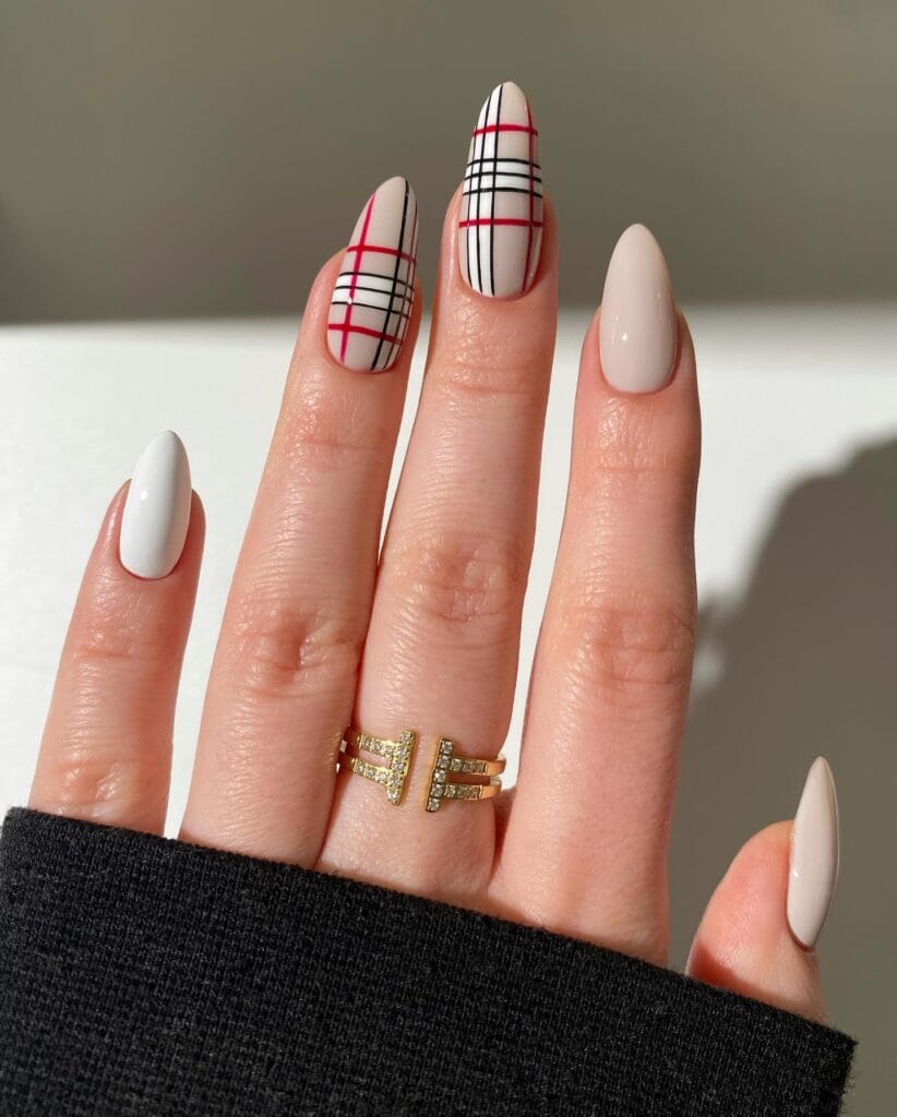 Neutral January nails with red-and-black plaid line art on two nails paired with creamy white almond nails.