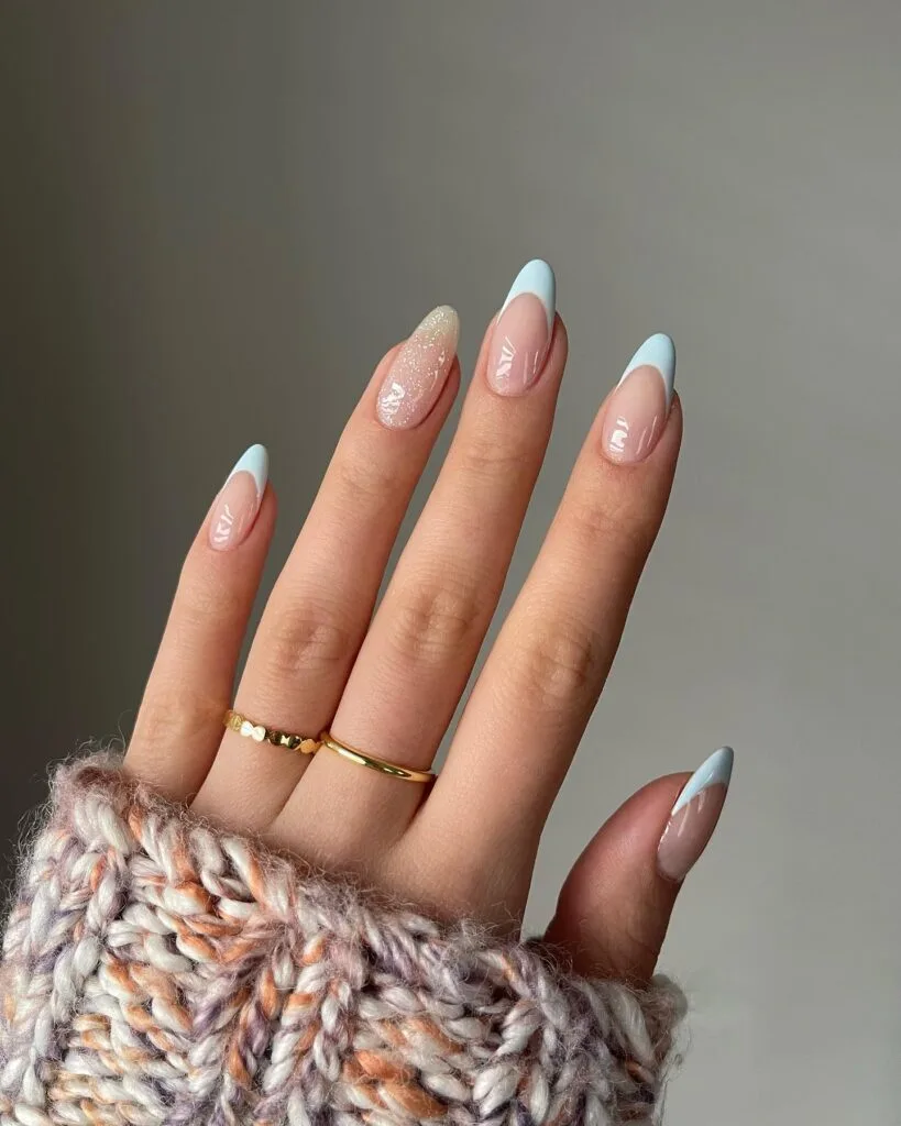 Simple winter nails with baby blue French tips and one glitter accent nail on almond shape.
