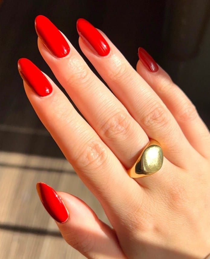orange-red almond nails with glossy finish and gold dome ring