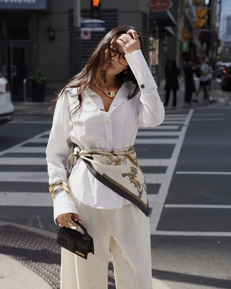 2026 fashion trends, white shirt with scarf styled as belt, cream pants, gold jewelry, structured black handbag