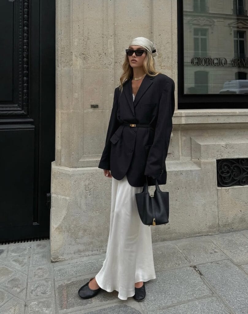 2026 fashion trends, oversized black blazer belted at waist, white maxi skirt, chunky gold chain necklace, black tote bag