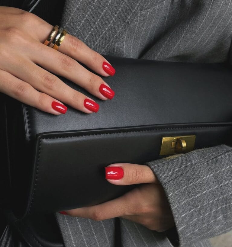 old money nails in glossy bright red on short nails holding black leather clutch