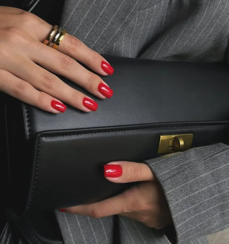 old money nails in glossy bright red on short nails holding black leather clutch