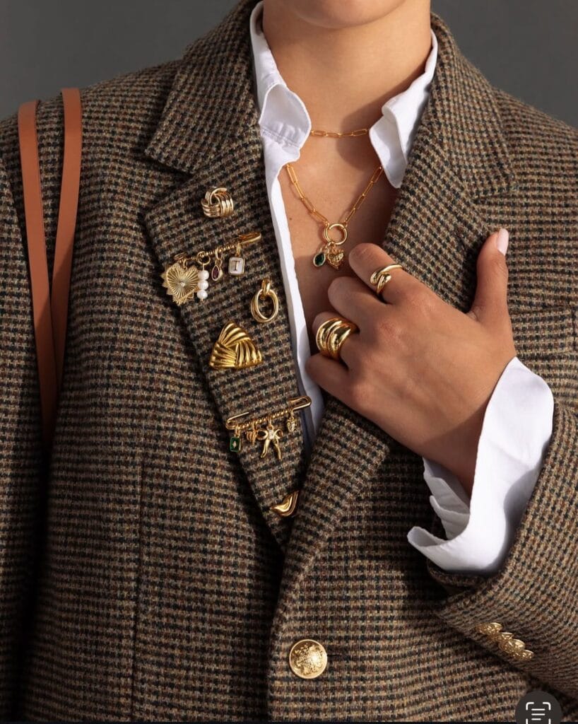 fashion trends 2026, houndstooth blazer with multiple gold brooches, layered necklaces and rings
