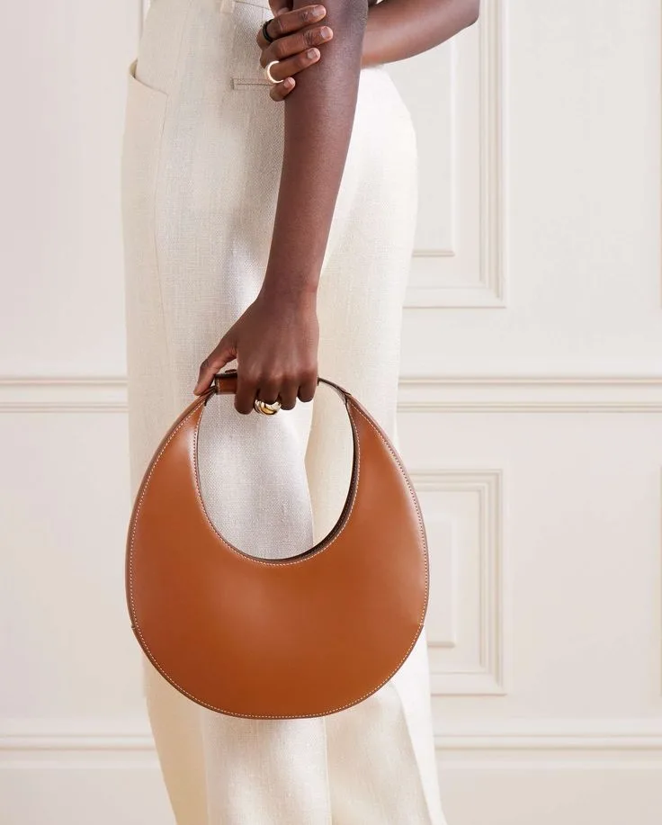 fashion trends 2026, tan leather crescent-shaped handbag with circular handle, sculptured bag