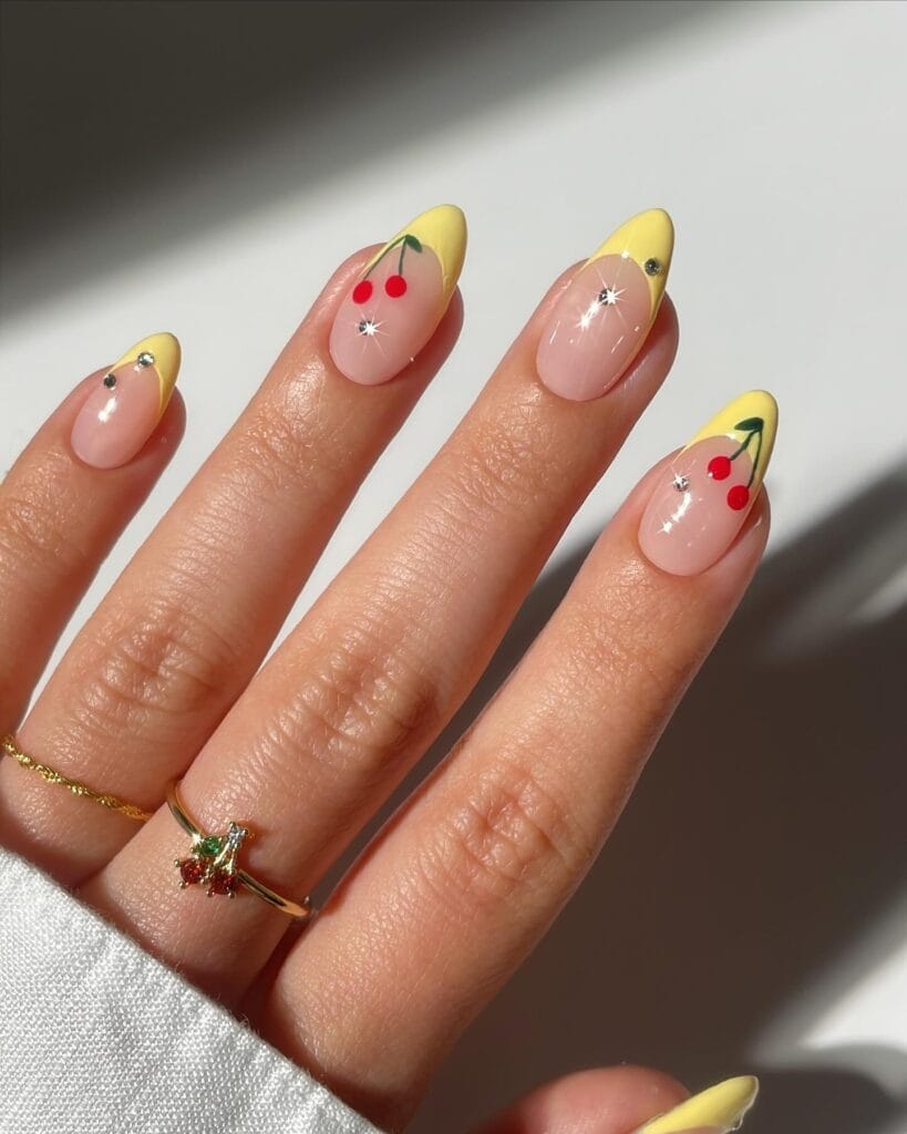 classy spring nails, almond nude nails with yellow French tips and red cherry accents with rhinestones