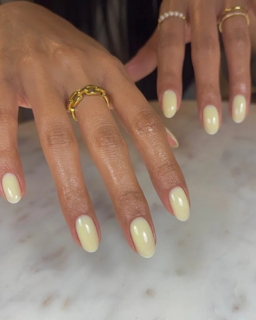 spring nail colors 2026, butter yellow almond nails with gold chain ring, glossy finish