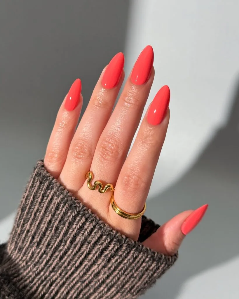 spring nail colors 2026, coral almond nails with gold wave ring, glossy finish
