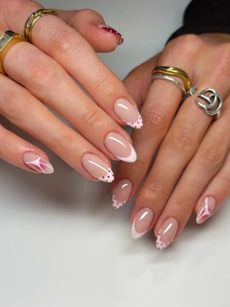 may nails, almond nude nails with white French tips and red polka dots plus pink abstract swirl accents
