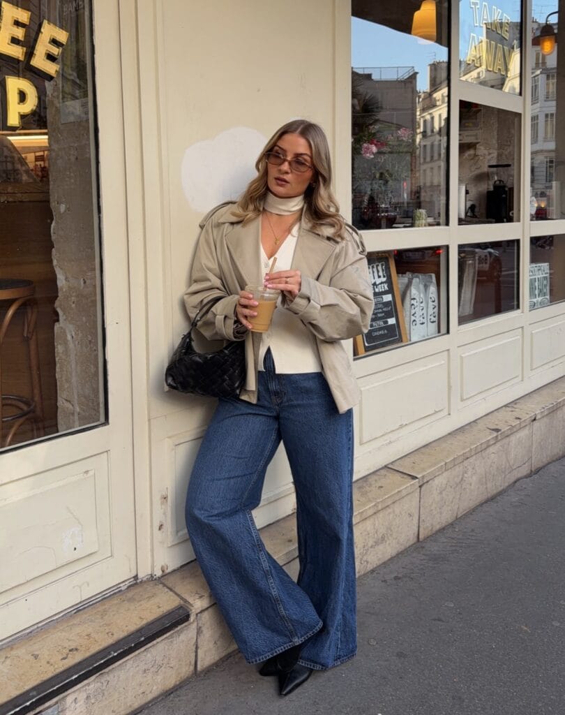 may outfit with beige cropped trench coat, cream button-down top, dark wash wide-leg jeans, and black pointed boots
