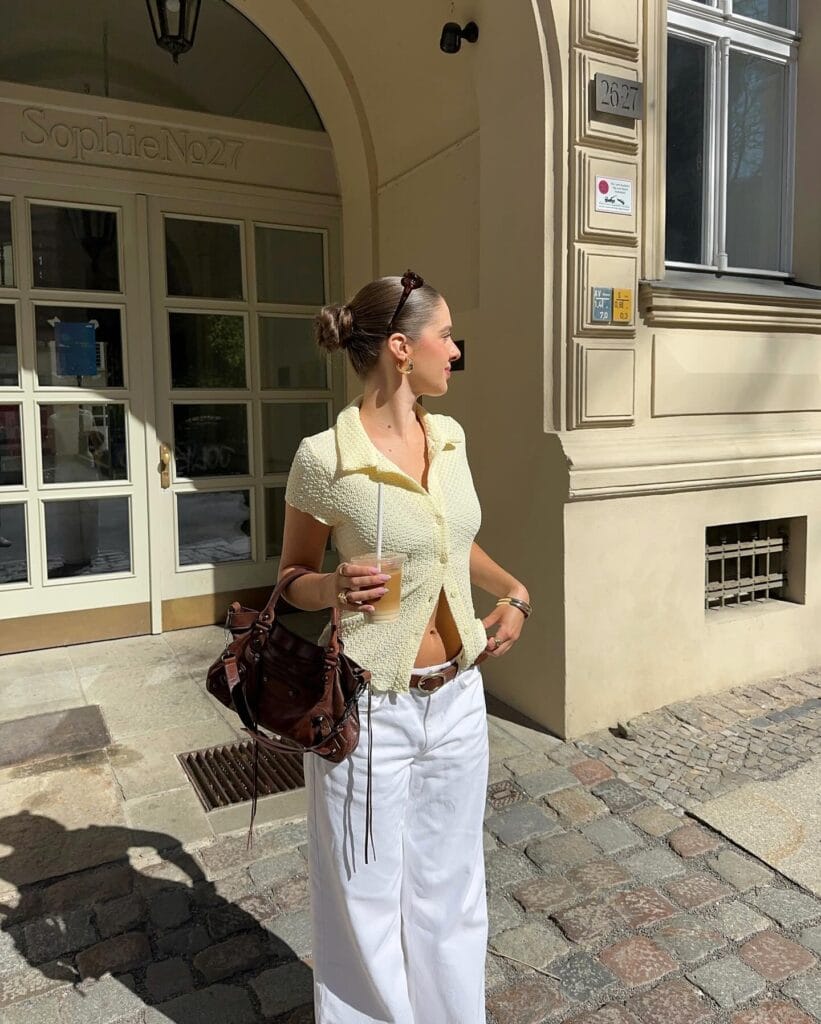 may outfit with yellow short-sleeve tweed top, white wide-leg trousers, brown leather belt, and brown leather bag
