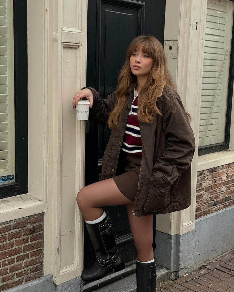 may outfit with brown oversized field jacket, striped rugby top, brown mini skirt, and black knee-high boots
