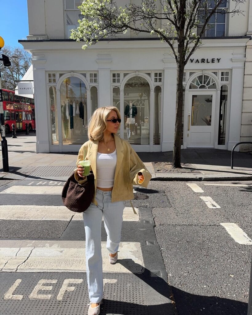 may outfit with tan open-front jacket, white tank top, light wash cuffed jeans, brown woven tote bag, and woven flats