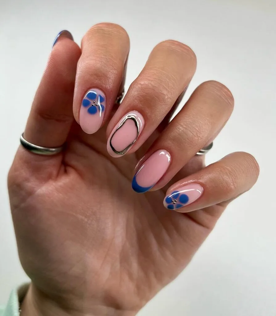 may nails, almond nude pink nails with cobalt blue French tips, blue floral accents, rhinestones, and chrome outline
