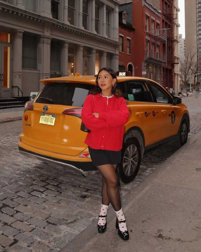 spring fashion trends 2026, red knit cardigan buttoned over white collared shirt and black mini skirt