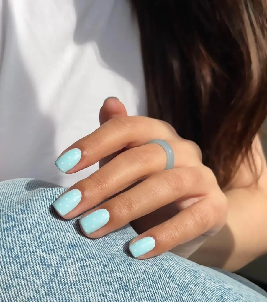 may nails, short square glossy baby blue nails with small white polka dot accents

