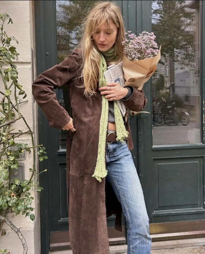 spring fashion trends 2026, long green knit scarf layered over brown suede coat with jeans