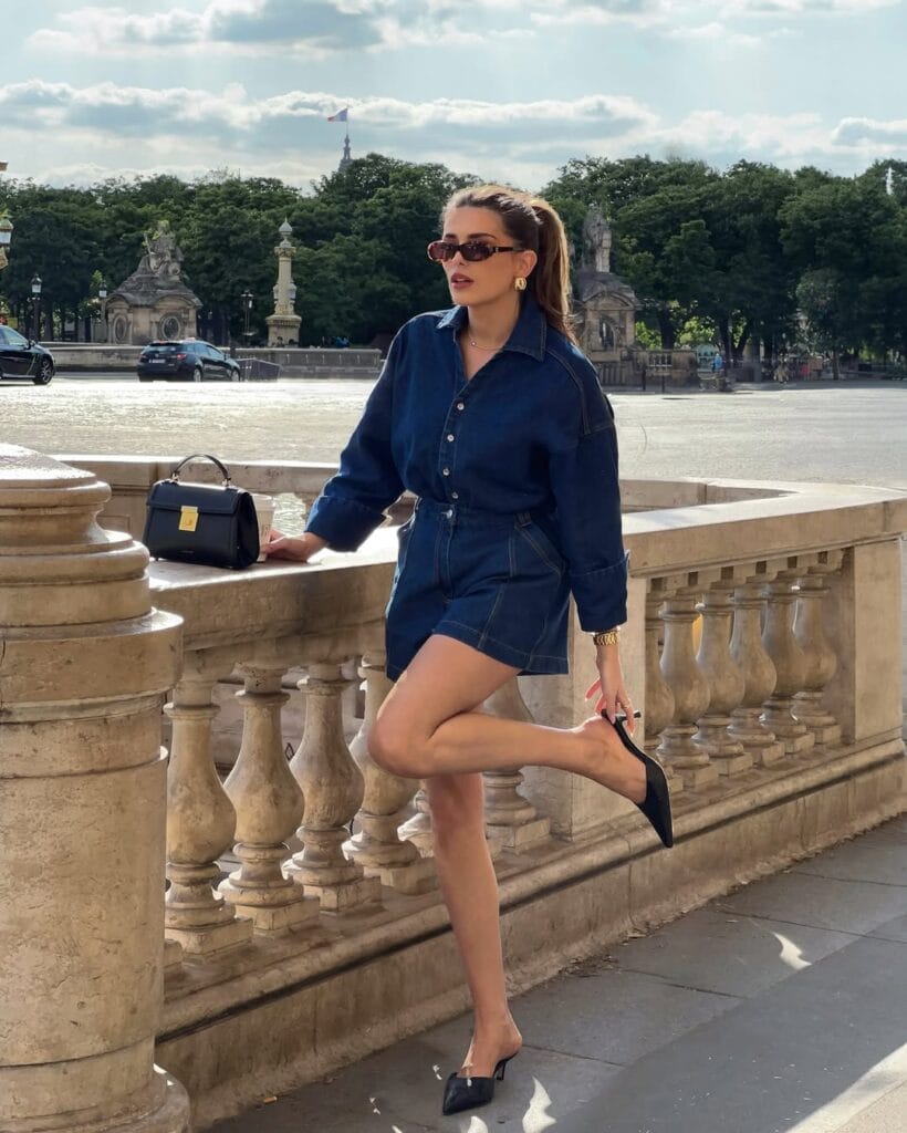 may outfit with dark wash denim romper, black pointed mule heels, and black structured handbag
