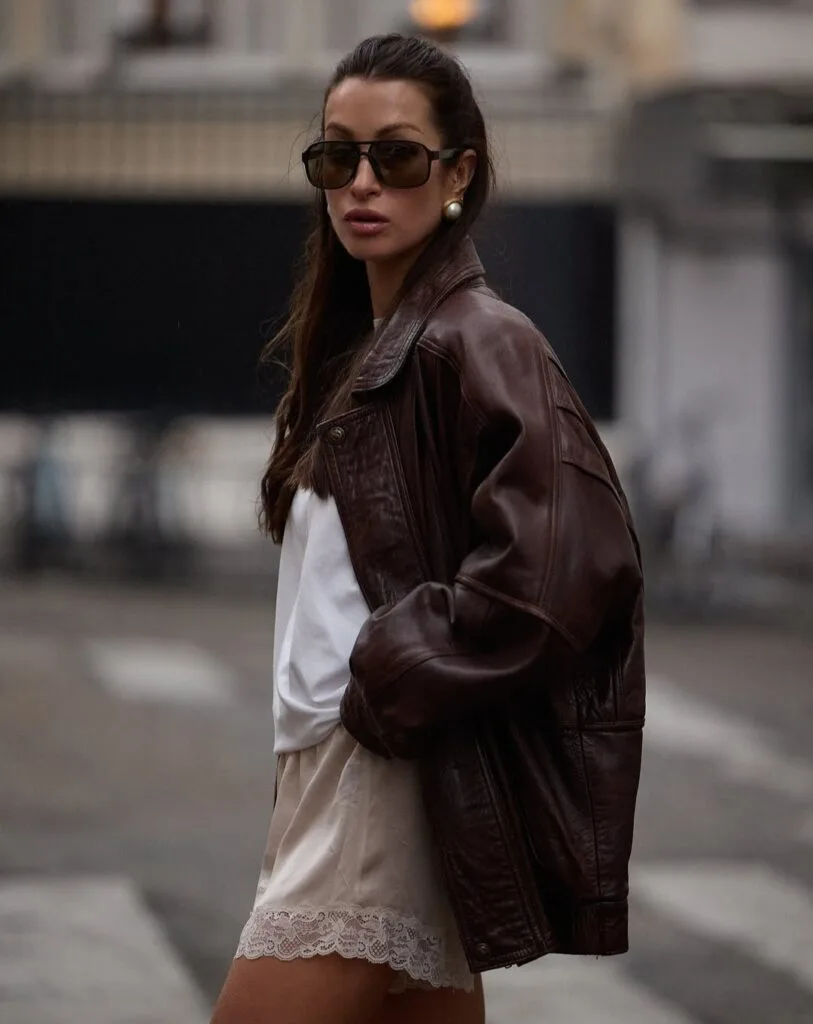 spring fashion trends 2026, cream lace-trimmed mini dress under brown leather jacke