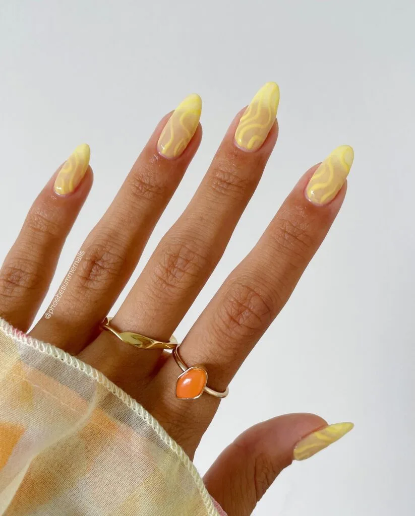 june nail color trends, yellow swirl nail art on sheer base with almond shape