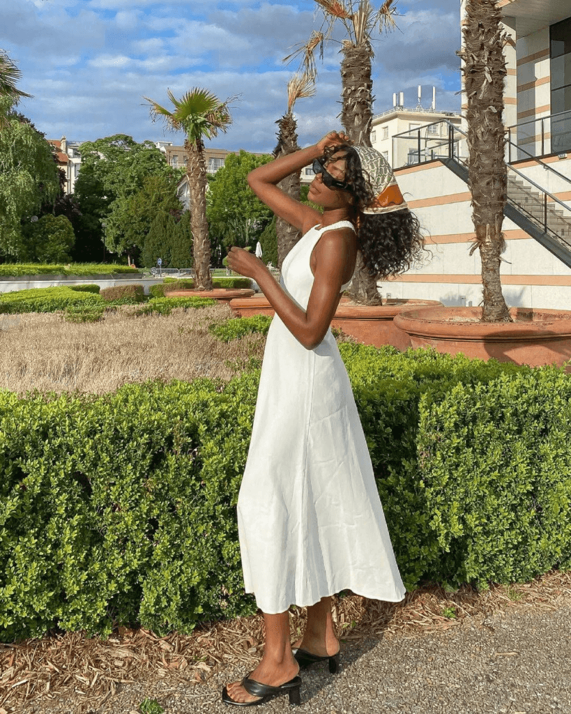 summer fashion trends 2026, white sleeveless midi dress with black heeled mule sandals and patterned cap