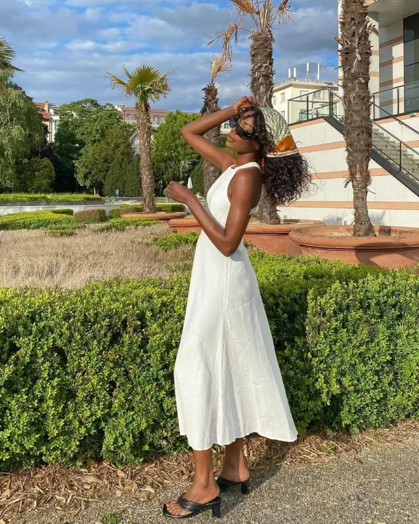 summer fashion trends 2026, white sleeveless midi dress with black heeled mule sandals and patterned cap