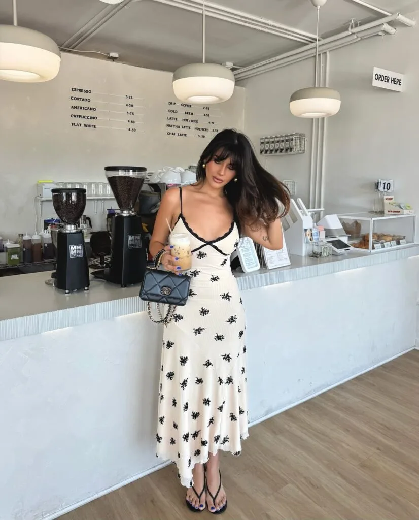 june outfit with cream and black floral print lace-trim midi dress, black heeled thong sandals, and black chain bag
