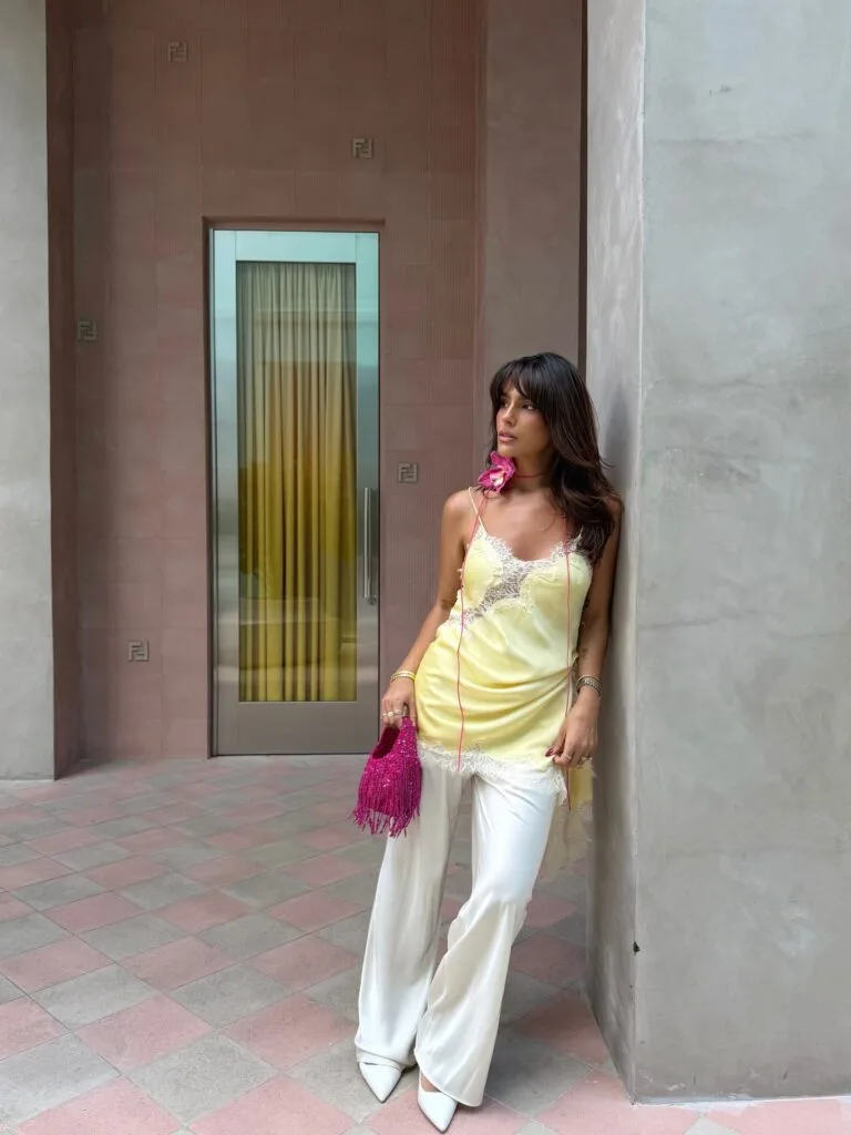 summer outfit with yellow lace-trim slip cami, white wide-leg trousers, white pointed pumps, and pink fringe bag
