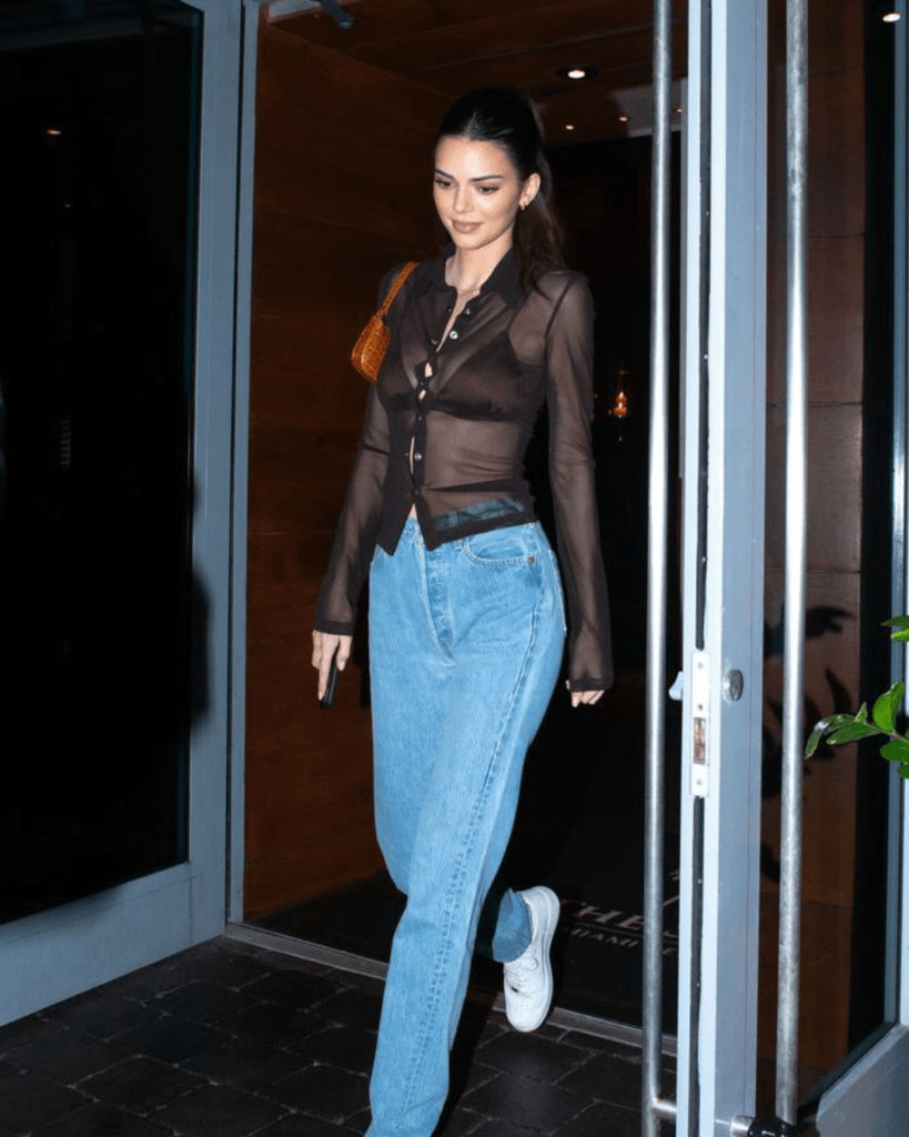 summer fashion trends 2026, sheer dark brown button-up shirt layered over bra with light wash jeans