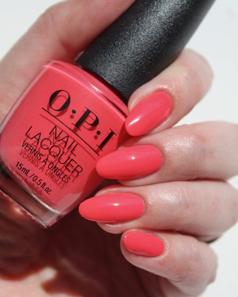 summer nail colors, bright coral glossy almond nails holding OPI polish bottle