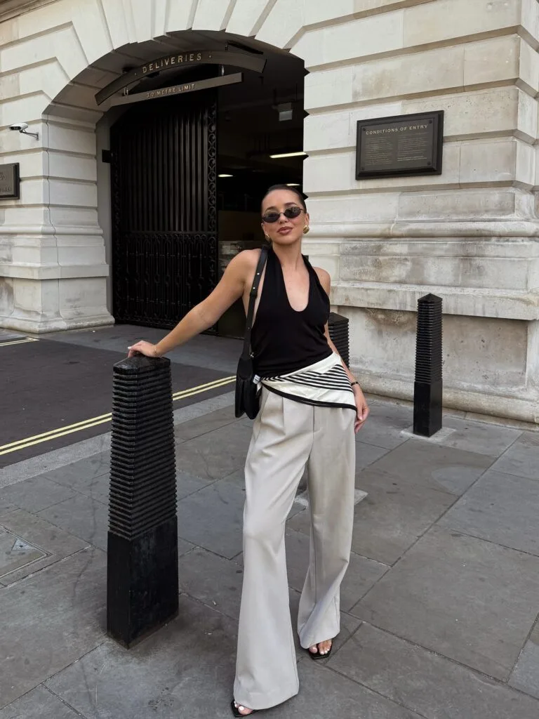  june outfit with black halter top, cream wide-leg trousers, striped scarf at waist, and peep-toe sandals
