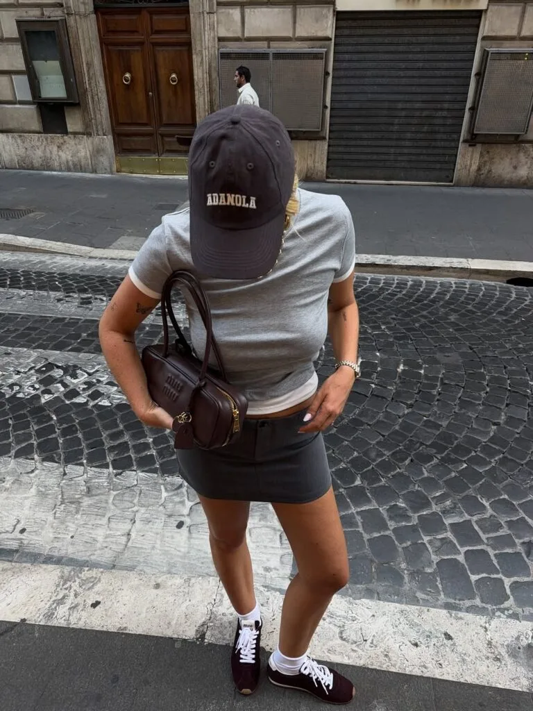 june outfit with grey fitted tee, charcoal mini skirt, brown baseball cap, and burgundy retro sneakers

