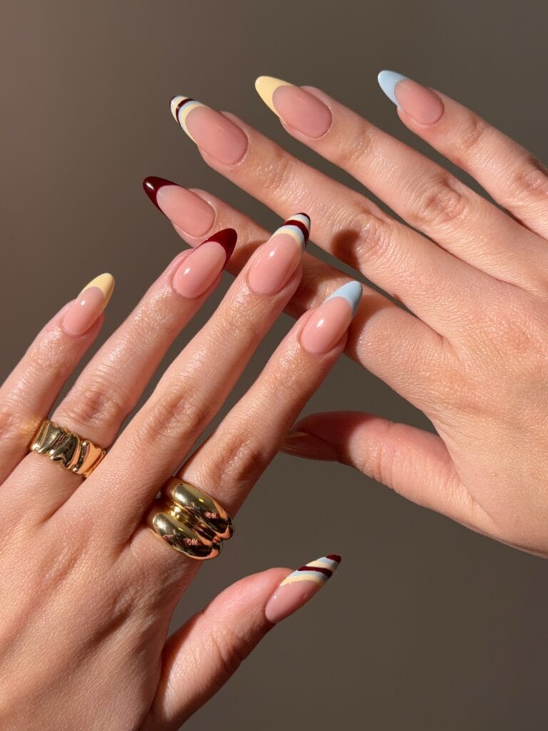 July nail ideas, nude almond nails with mismatched French tips in yellow blue burgundy and stripes
