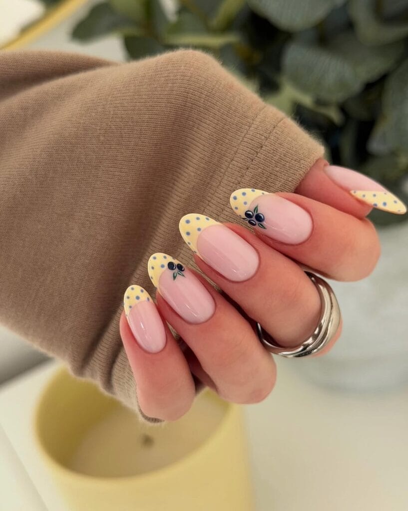June nail ideas, butter yellow French tip almond nails with blueberry art and blue polka dots
