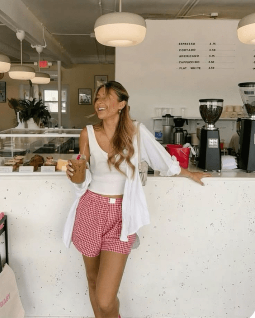 summer fashion trends 2026, red gingham boxer shorts with white tank top and open white button-down at coffee shop