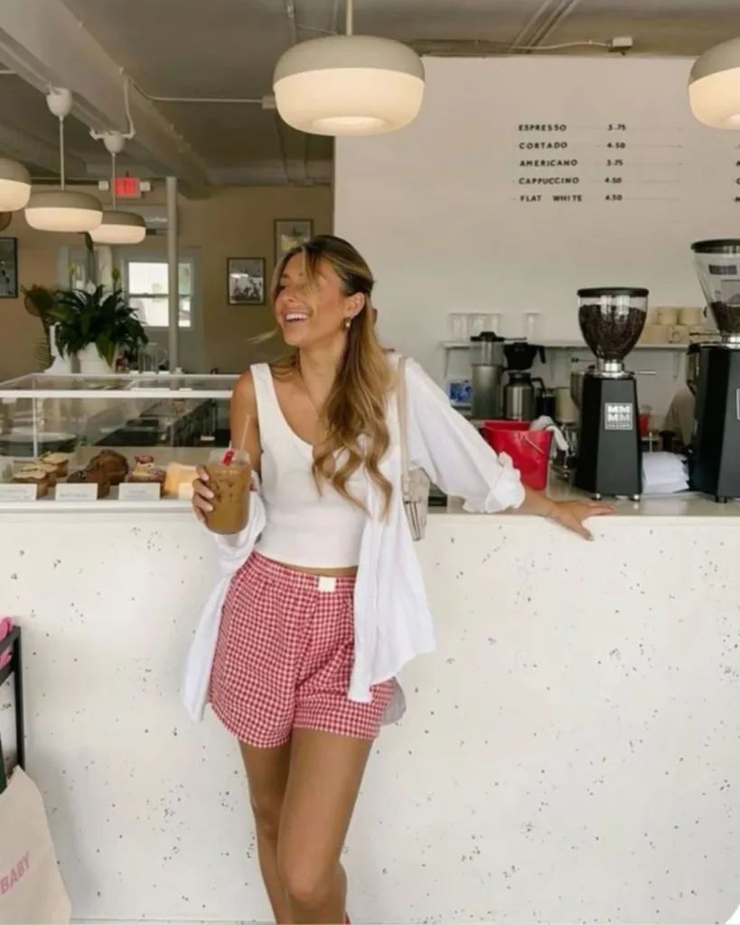 summer fashion trends 2026, red gingham boxer shorts with white tank top and open white button-down at coffee shop