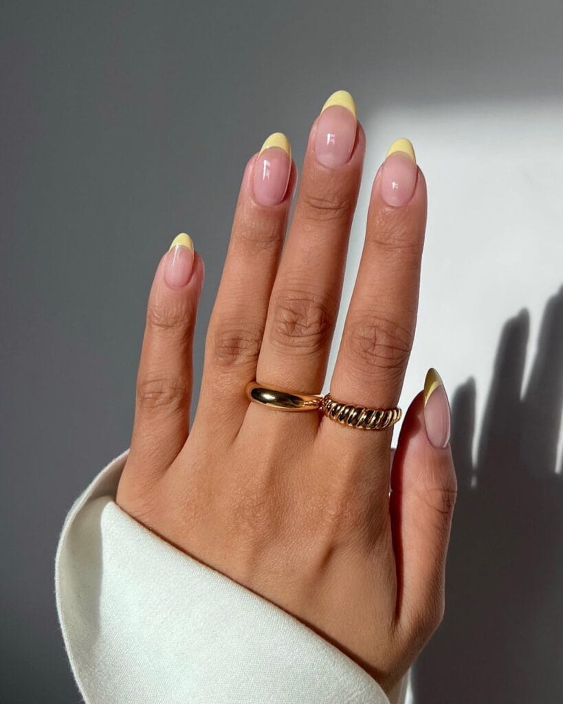 June nail color trends, pastel yellow French tip almond nails on glossy nude base