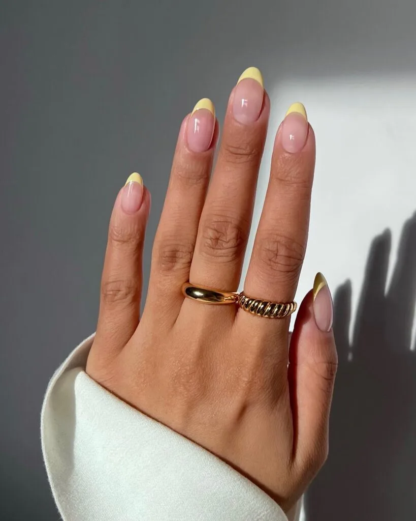 June nail color trends, pastel yellow French tip almond nails on glossy nude base