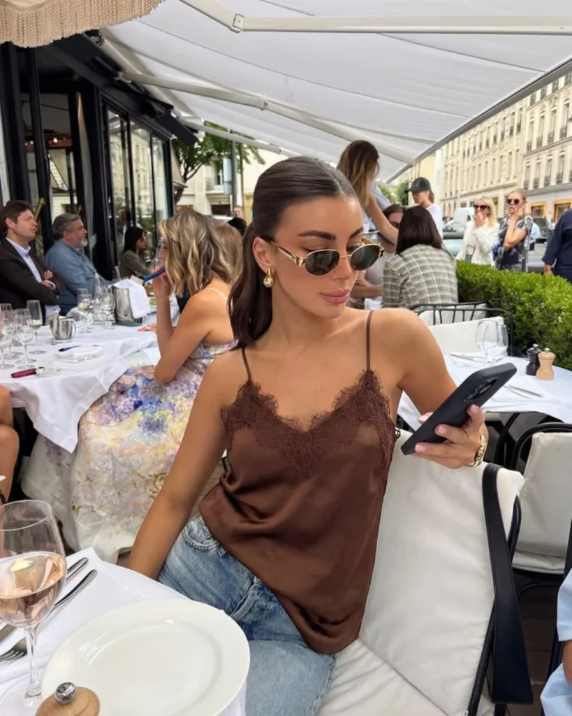 summer fashion trends 2026, brown satin lace-trim cami with light wash jeans at outdoor café