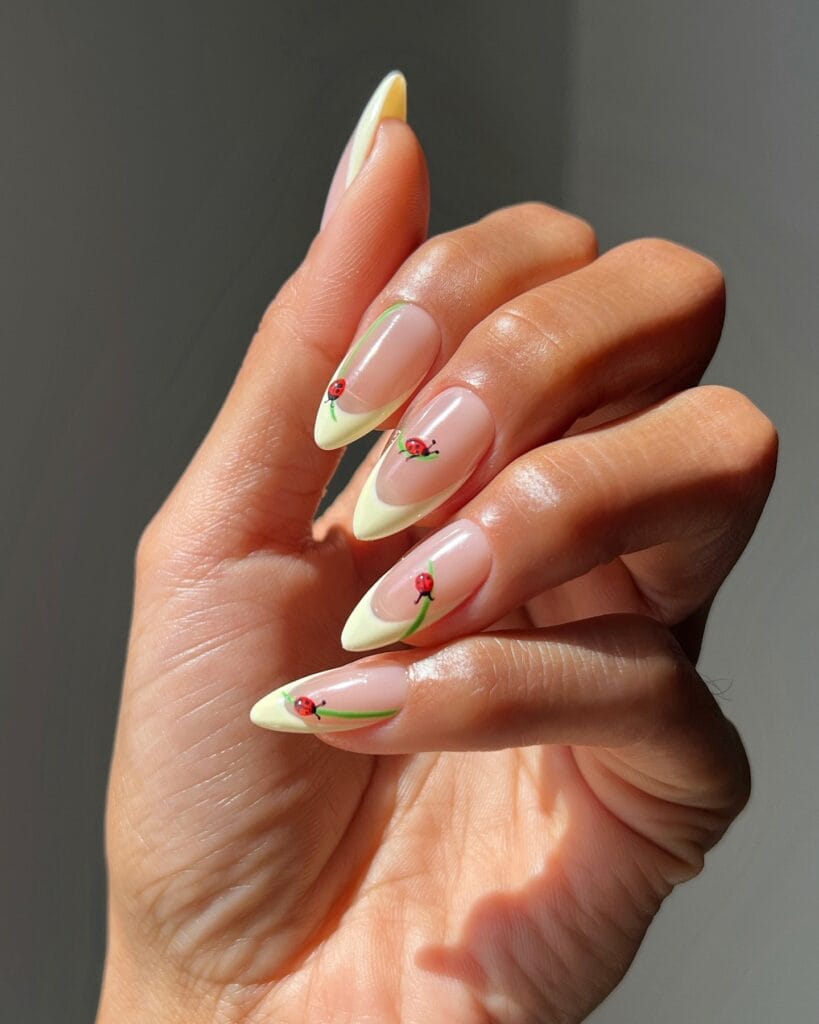 July nail ideas, nude almond nails with butter yellow French tips and tiny red ladybug on green stem art